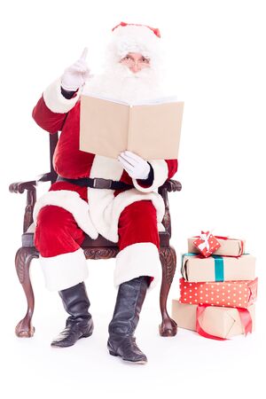 Portrait of santa Claus sitting in chair and reading a book on white backgroundの写真素材