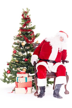 Portrait of Santa Claus sleeping in chair next to Christmas tree, heap of gift boxes near himの写真素材