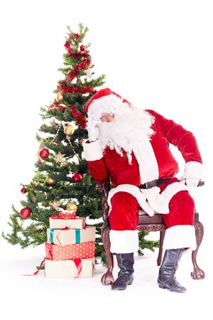 Portrait of Santa Claus sleeping in chair next to Christmas tree, heap of gift boxes near himの写真素材