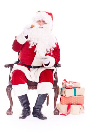 Portrait of Santa Claus sitting in chair and eating cookies isolated on whiteの写真素材