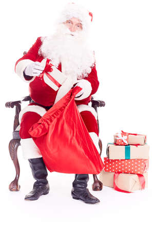 Portrait of santa Claus sitting in chair and putting Christmas giftboxes into red sackの写真素材