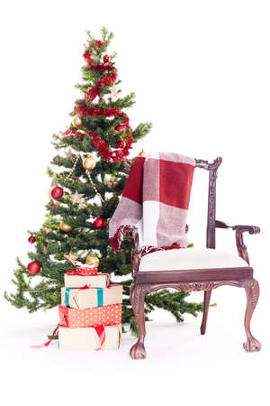 Empty chair with blanket on it near Christmas tree and stack of gift boxes on white backgroundの写真素材