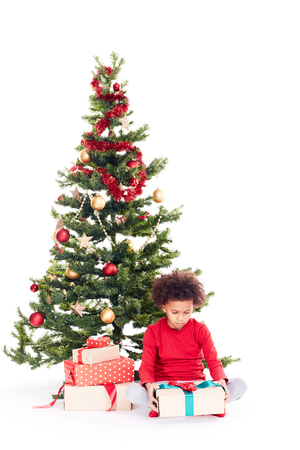 Portrait of cute mixed race little boy sitting on floor near Christmas tree with gift box in his handsの写真素材