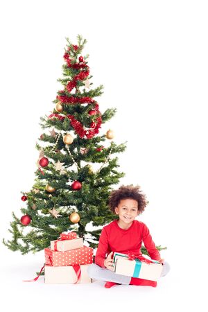 Portrait of cute mixed race little boy sitting on floor near Christmas tree with gift box in his handsの写真素材