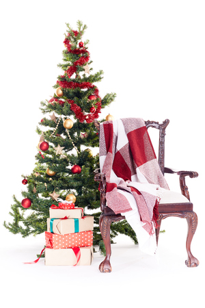 Empty chair with blanket on it near Christmas tree and stack of gift boxes on white backgroundの写真素材