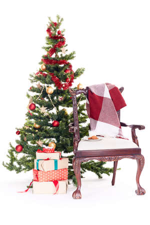Empty chair with blanket on it near Christmas tree and stack of gift boxes on white backgroundの写真素材