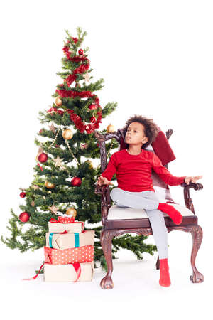 Portrait of cute mixed race little boy sitting in chair near Christmas treeの写真素材
