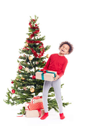Portrait of cute mixed race little boy standing near Christmas tree with gift box in his handsの写真素材