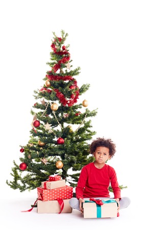 Portrait of cute mixed race little boy sitting on floor near Christmas tree with gift box in his handsの写真素材