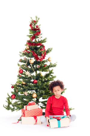 Portrait of cute mixed race little boy sitting on floor near Christmas tree with gift box in his handsの写真素材