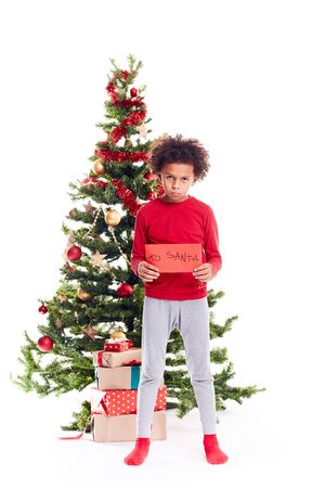 Portrait of cute mixed race little boy standing near Christmas tree holding letter to Santaの写真素材