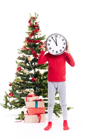 Portrait little boy standing near Christmas tree holding clock showing five minutes to twelveの写真素材