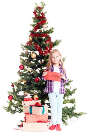 Portrait of little girl standing near Christmas tree with letter to Santa in her hands on white backgroundの写真素材