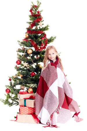 Portrait of little girl wrapped in blanket standing near Christmas tree on white backgroundの写真素材