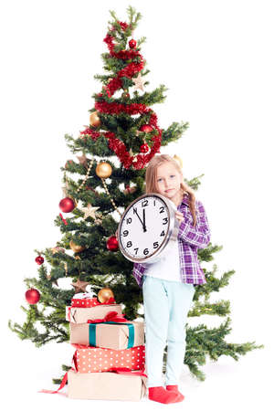 Portrait of little girl with clock showing five minutes to twelve standing near Christmas tree on white backgroundの写真素材