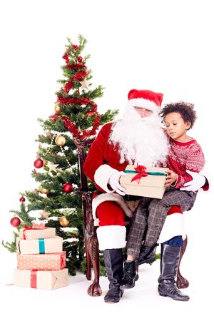 Mixed-race little boy receiving Christmas gift from Santa Claus while sitting on his lapの写真素材