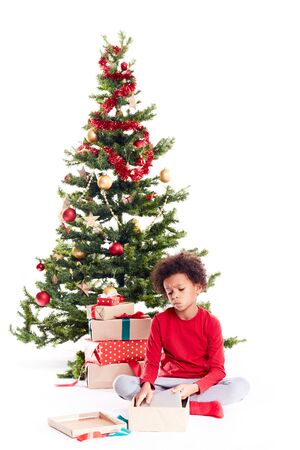 Portrait of cute mixed race little boy unpacking gifts near Christmas tree and taking digital tablet out of boxの写真素材