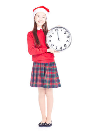 Isolated portrait of girl wearing school uniform and Santa hat holding clock showing twelveの写真素材