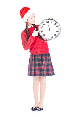Isolated portrait of girl wearing school uniform and Santa hat holding clock showing twelveの写真素材