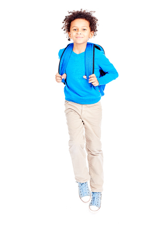 Portrait of cute curly-haired Latin American boy with backpack walking to schoolの写真素材