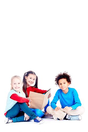 Three multi-ethnic elementary students sitting on floor and reading a book togetherの写真素材