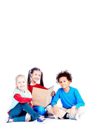Three multi-ethnic elementary students sitting on floor and reading a book togetherの写真素材