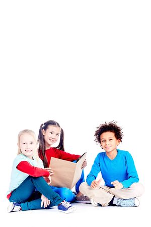 Three multi-ethnic elementary students sitting on floor and reading a book togetherの写真素材