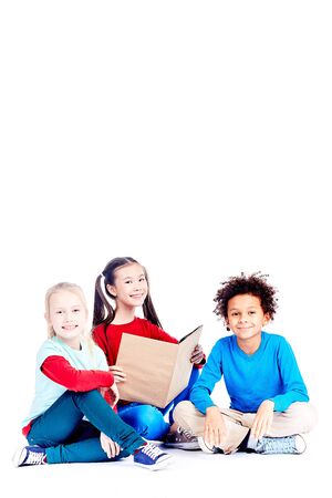 Three multi-ethnic elementary students sitting on floor and reading a book togetherの写真素材