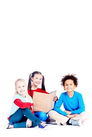 Three multi-ethnic elementary students sitting on floor and reading a book togetherの写真素材