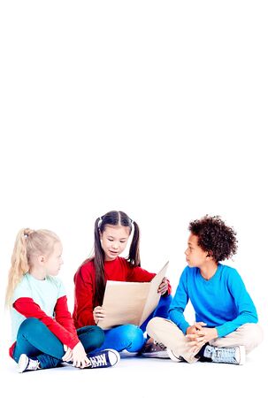 Three multi-ethnic elementary students sitting on floor and reading a book togetherの写真素材