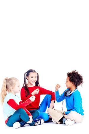 Three diverse elementary students sitting on floor and playing rock paper scissors gameの写真素材