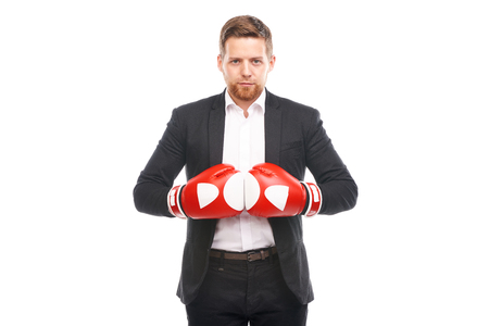 Studio portrait of young businessman in white shirt and suit wearing red boxing gloves on white backgroundの写真素材