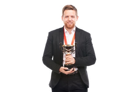 Portrait of confident young businessman wearing medal and holding trophy on white backgroundの写真素材