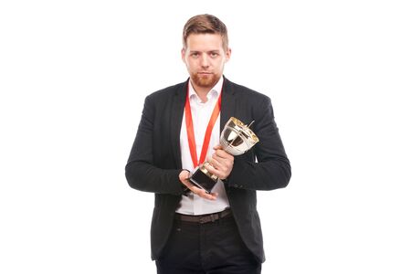 Portrait of confident young businessman wearing medal and holding trophy on white backgroundの写真素材