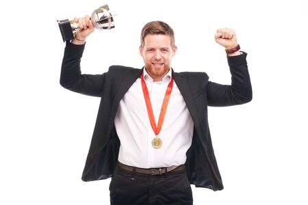 Portrait of confident young businessman wearing medal and holding trophy on white backgroundの写真素材