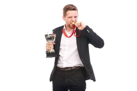 Portrait of confident young businessman wearing medal and holding trophy on white backgroundの写真素材