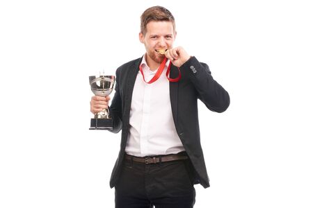 Portrait of confident young businessman wearing medal and holding trophy on white backgroundの写真素材