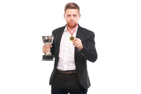 Portrait of confident young businessman wearing medal and holding trophy on white backgroundの写真素材