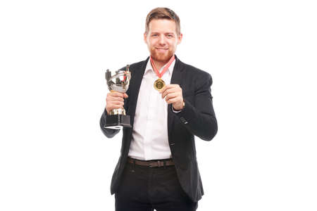 Portrait of confident young businessman wearing medal and holding trophy on white backgroundの写真素材