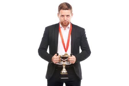 Portrait of confident young businessman wearing medal and holding trophy on white backgroundの写真素材