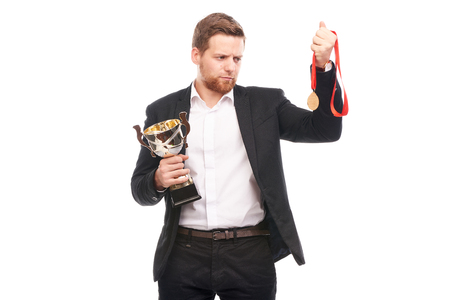 Portrait of confident young businessman wearing medal and holding trophy on white backgroundの写真素材