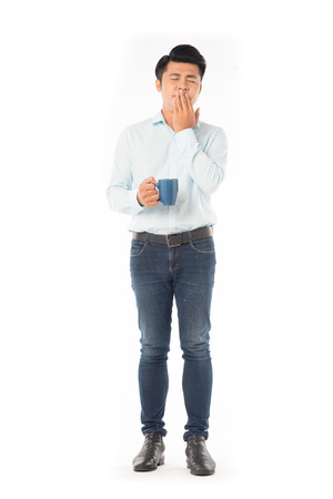 Young Asian man holding mug with hot drink on white backgroundの写真素材