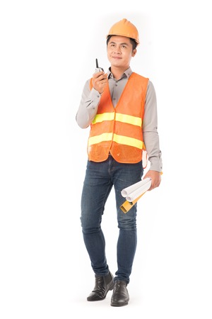 Studio portrait of construction worker in orange waistcoat and hardhat using walkie-talkieの写真素材