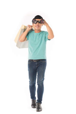 Portrait of young Asian man carrying shopping bag and watching through binoculars isolated on whiteの写真素材
