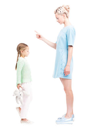 Vertical full length isolated side view shot of young adult woman scolding her daughter for being naughty, white backgroundの写真素材
