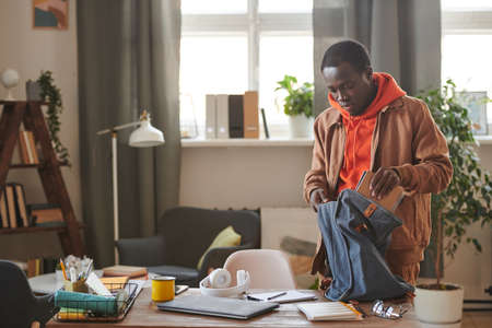Stylish African American college student wearing casual clothes getting ready for school putting textbooks and copybooks into backpack, copy spaceの写真素材