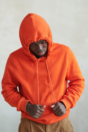 Vertical medium studio conceptual portrait of young African American man wearing orange hoodie...