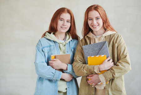 Horizontal medium studio portrait of two modern twin college students wearing casual clothes holding textbooks smiling at cameraの写真素材