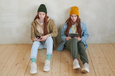 High angle view studio portrait of young twin sisters wearing fashionable casual clothes sitting on...