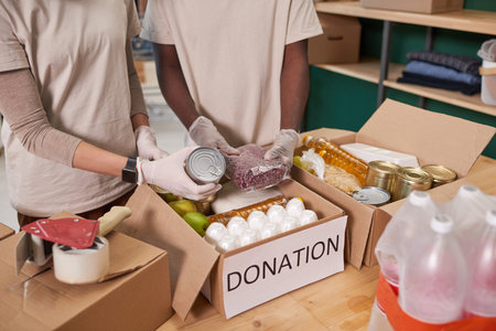 High angle shot of unrecognizable volunteers wearing protective gloves packing food supplies into...